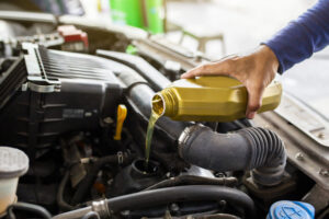 Car mechanic replacing and pouring fresh oil into engine at maintenance repair service station.